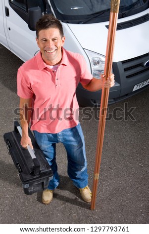 Portrait of smiling plumber holding toolbox standing next to van