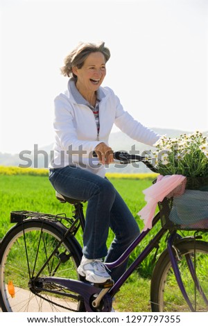 Smiling senior woman riding bike with basket of flowers in countryside
