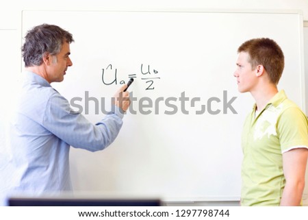 Teacher and male high school student look at equation on whiteboard