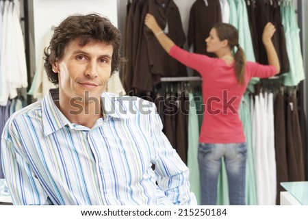 Couple shopping in clothes shop, woman choosing clothes, man smiling in foreground, portrait