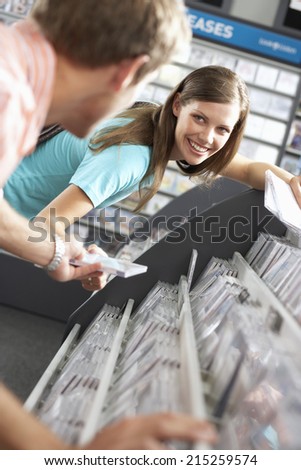 Young man passing CD to woman in record shop, bending down, smiling, side view, focus on background (tilt)