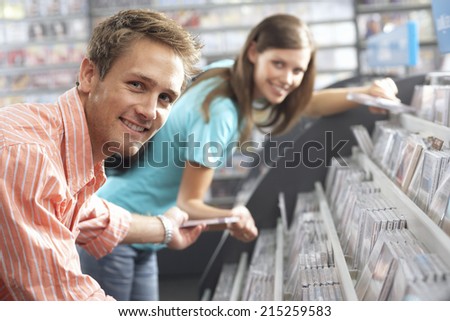 Young man passing CD to woman in record shop, bending down, smiling, side view, portrait