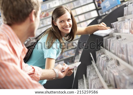 Young man passing CD to woman in record shop, bending down, smiling, side view, focus on background (tilt)