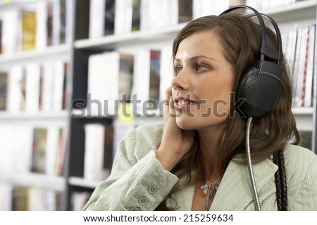Young woman wearing headphones, listening to CDs in record shop, smiling, close-up, side view
