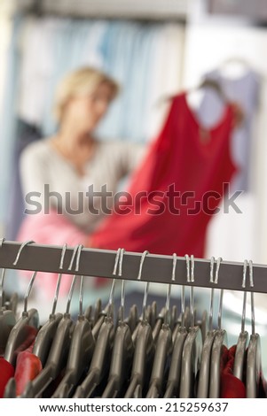 Mature woman shopping in clothes shop, holding red top, focus on clothes rail in foreground (tilt)