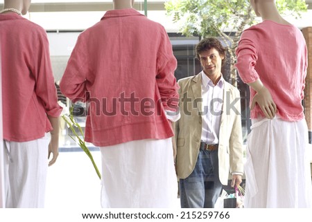 Man window shopping, looking at three mannequins wearing pink tops and white skirts in clothes shop