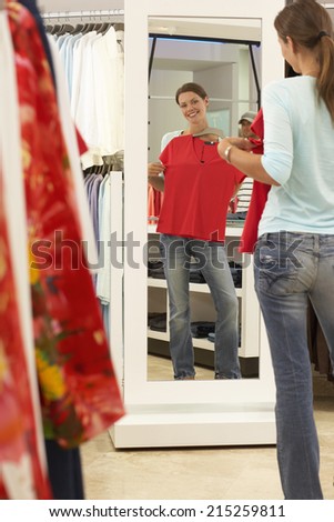 Woman trying on red top in clothes shop, looking at reflection in mirror, smiling, rear view