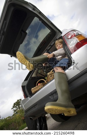 Boy (8-10) putting on wellington boots, sitting in boot of stationary car, smiling, portrait, low angle view (tilt)