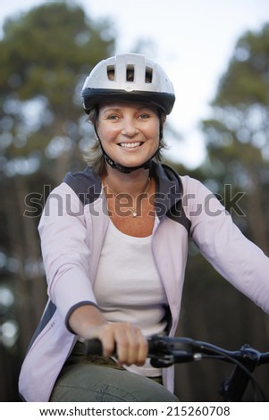 Woman wearing cycling helmet and pink hooded sports top, sitting on bicycle, smiling, portrait
