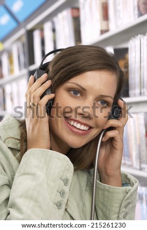 Young woman wearing headphones, listening to CDs in record shop, smiling, close-up