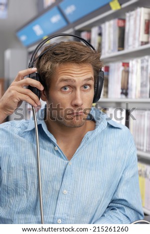Young man wearing headphones, listening to CDs in record shop, looking disappointed, close-up, portrait