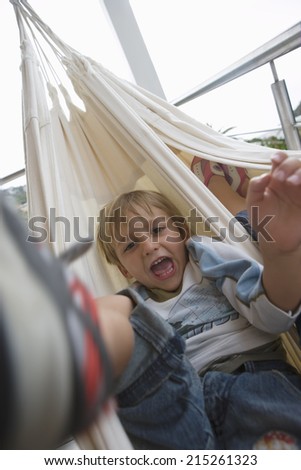 Boy (6-8) lying in hammock, mouth open, front view, close-up, portrait (blurred motion, tilt)