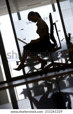 Silhouette of businesswoman sitting in office chair, using laptop, profile, surface level (tilt)