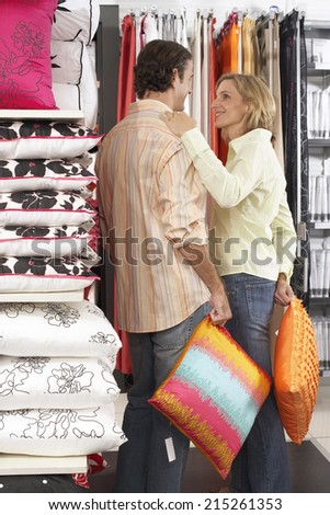 Couple shopping for cushions in department store, woman placing hand on man\'s shoulder, smiling