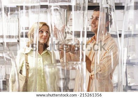 Couple shopping for glass vases in department store, woman raising eyebrows, man smiling