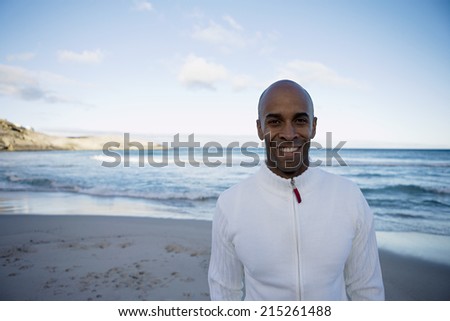 Man in white top standing on beach at sunset, smiling, front view, portrait, sea in background