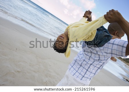 Father carrying daughter (5-7) on shoulders on beach, girl upside down, smiling, rear view (tilt)
