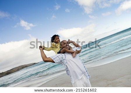 Father carrying daughter (5-7) on shoulders, walking on beach, smiling, side view (tilt)