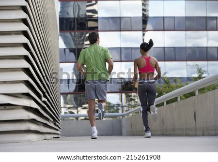 Couple jogging on urban elevated walkway, running side by side, rear view, surface level