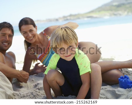 Two generation family sitting on beach, smiling, boy (5-7) crouching in foreground, portrait