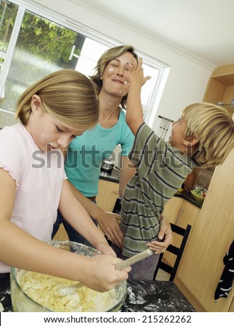 Boy (5-7) rubbing flour onto mother\'s face in kitchen, girl (6-8) stirring cake mix in bowl (tilt)