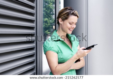 Young woman in green short-sleeved blouse text messaging on mobile phone, smiling, side view