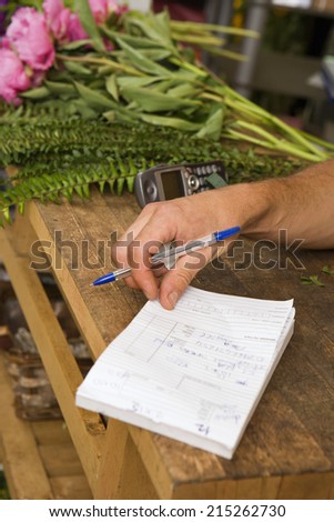 Florist writing in order pad beside bunch of flowers in flower shop, close-up, side view