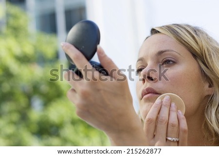 Young blonde woman applying make-up using powder compact, close-up