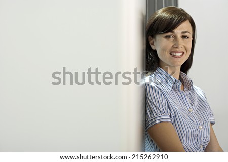 Businesswoman standing beside office window, smiling, side view, portrait