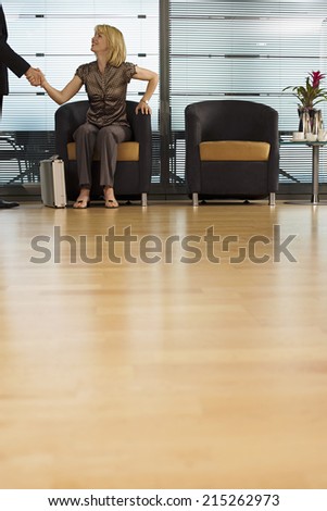 Businesswoman sitting in office reception area, shaking hands with businessman, surface level