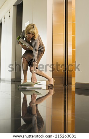 Businesswoman standing beside office elevator, picking up folder from floor, surface level