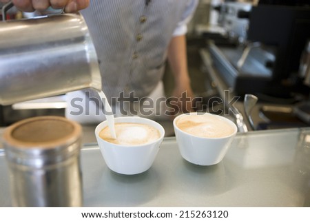 Waiter making two lattes, pouring milk from jug into cups, mid-section, close-up