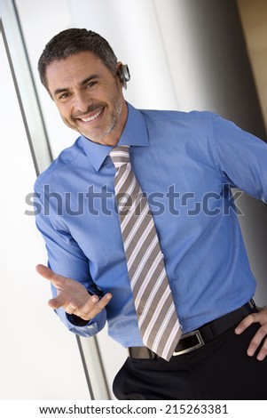 Businessman wearing mobile phone hands-free device, making hand sign, smiling, portrait (tilt)