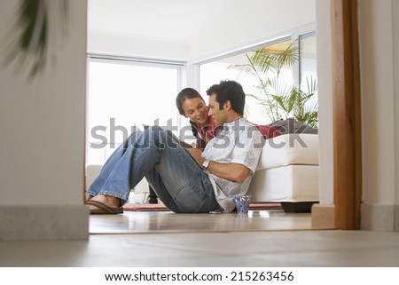 Couple relaxing at home, man sitting on floor, woman on sofa, surface level, view through doorway