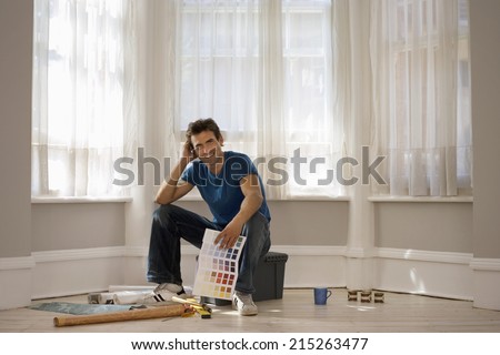 Man decorating at home, sitting on floor beside window, holding colour swatch, smiling, portrait