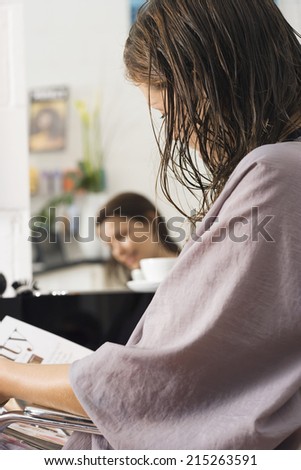 Woman sitting in hair salon, reading magazine in lap, side view, reflection in mirror
