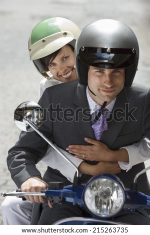 Couple in crash helmets riding on scooter in street, smiling, front view, portrait