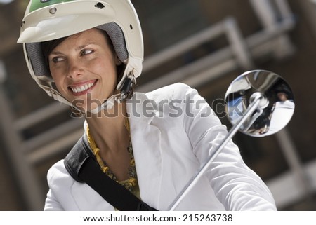 Woman in crash helmet riding on scooter in street, smiling, front view, close-up (tilt)