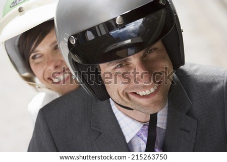 Couple in crash helmets riding on scooter in street, smiling, front view, close-up, portrait