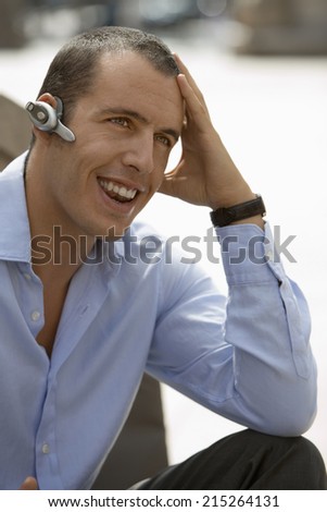 Businessman wearing mobile phone hands-free device on ear, smiling, close-up, outdoors