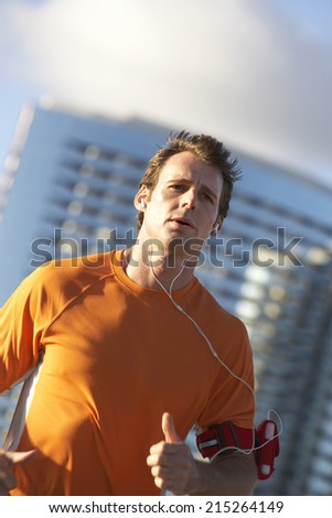 Man wearing orange t-shirt, jogging in city, listening to MP3 player strapped to arm, close-up (tilt)