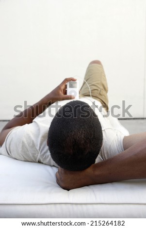 Man relaxing at home, lying on back, listening to MP3 player, rear view