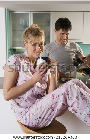 Couple sitting at kitchen breakfast bar, woman with feet up, man pouring coffee from cafetiere