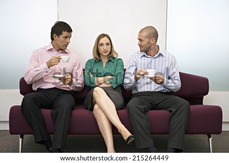 Businesswoman sitting between two businessmen on sofa, men holding cups and saucers, front view
