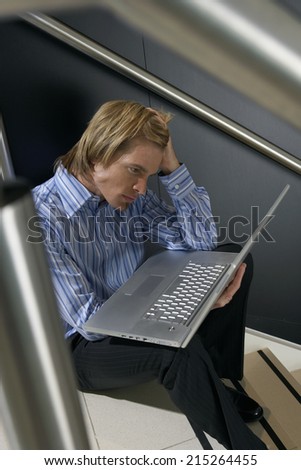 Businessman sitting on staircase, using laptop in lap, leaning head on hand, thinking, side view