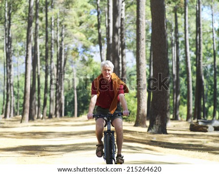 Active senior man cycling through woodland, smiling, front view, portrait