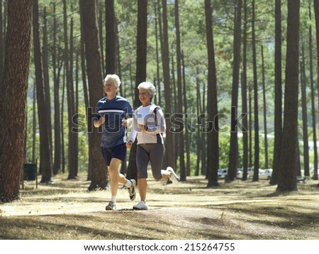 Senior couple in sportswear jogging through woodland, smiling