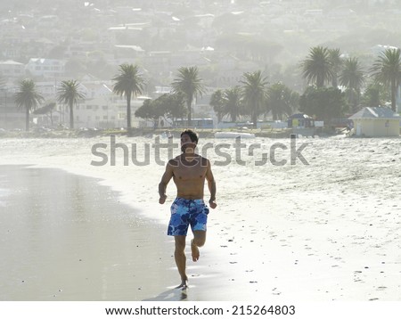 South Africa, Cape Town, man in swimming shorts jogging along sandy beach