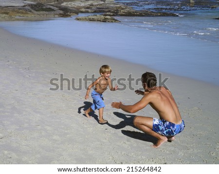 Father and son (4-6) playing on beach, boy running into man\'s arms, smiling, elevated view