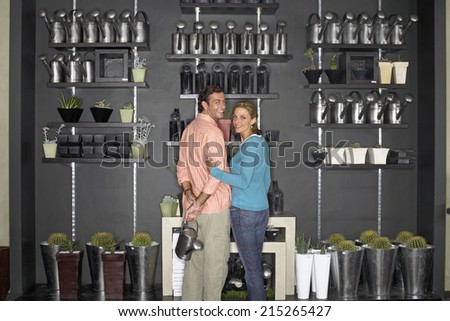 Couple standing beside cacti display in shop, man holding watering can, smiling, rear view, portrait